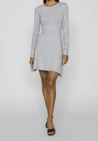 Robe grise à manches longues avec une coupe décontractée, un col arrondi et un ourlet asymétrique. Fabriquée à partir d'un tissu doux et texturé, portée avec des sandales noires.