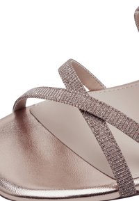 Metalické sandály ve zlaté růžové barvě s křížovými třpytivými pásky, hladkým, lesklým stélkou a kulatým designem špičky.