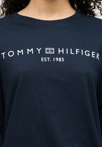 Σκούρο μπλε βαμβακερό t-shirt με λευκό κείμενο: "TOMMY HILFIGER" και "EST. 1985", σε casual στυλ με στρογγυλή λαιμόκοψη.