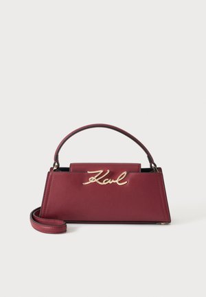 Petit sac à main structuré bordeaux avec une poignée supérieure et un logo en écriture dorée "Karl" sur le devant, avec une sangle supplémentaire pour le poignet.