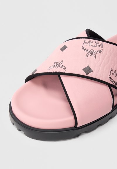 Lyserød slidesandal med en tekstureret overdel, sort gummisål og markante MCM-logoer i grå. Har et krydsbåndsdesign med sort kant.