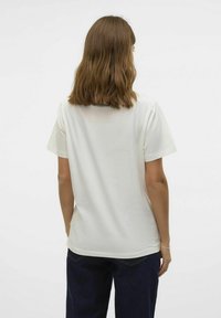 Lys beige t-shirt, korte ærmer, afslappet pasform, bomuldsstof, ensfarvet design, set fra ryggen, iført mørkeblå brede jeans.