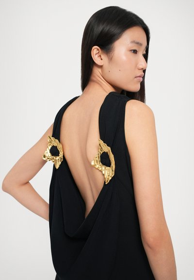 Vestido preto sem mangas com costas drapeadas, apresentando dois detalhes decorativos metálicos dourados nos ombros. Tecido suave, design de costas abertas.