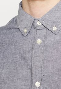 Light gray button-up shirt featuring a classic collar, smooth texture, and round plastic buttons along the front and collar.