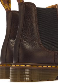 Paire de bottes en cuir marron foncé avec panneaux latéraux élastiques noirs, coutures jaunes au-dessus des semelles translucides rainurées et languettes à l'arrière.