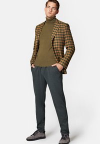 Brązowa i pomarańczowa kraciasta marynarka, oliwkowy golf, ciemnoszare spodnie i szare zamszowe buty. Dopasowany krój z teksturowanymi materiałami.