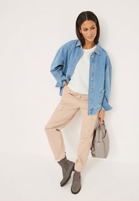 Veste en denim bleu clair, chemise rayée blanche, pantalon cargo beige, bottines grises et sac à main gris avec quincaillerie en argent.