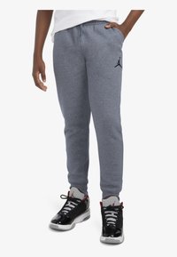 Pantalones de chándal grises con cintura elástica, bolsillos laterales y detalle del logo en negro. Llevados con zapatillas negras y blancas con acentos rojos.