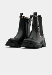 Botas de cuero negras hasta el tobillo con suela gruesa, presentan ojales en tono dorado, cremallera lateral y paneles elásticos para facilitar el calzado.