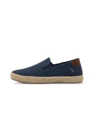 Zapato de slip-on azul marino con suela trenzada en tono beige y acento marrón en el talón, mostrado en perfil lateral sobre fondo blanco.