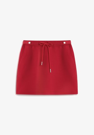 Falda deportiva roja hecha de una tela suave, con una cintura elástica y cordón, dos bolsillos laterales y accesorios metálicos.