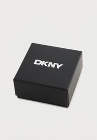 Crna kartonska kutija s mat završnom obradom, s DKNY logotipom u srebrnoj boji, kvadratnog oblika, čistog dizajna, bez dodatnih uzoraka ili akcenata.