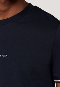 Navy cotton t-shirt with a crew neckline, featuring a white logo text on the chest and striped accents on the sleeve cuffs.