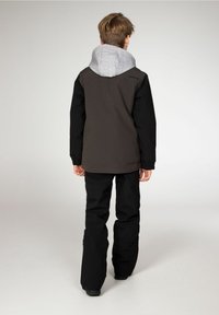 Giacca con cappuccio nera e grigia con maniche elastiche, abbinata a pantaloni neri. Il cappuccio ha una fodera interna grigia chiara e un taglio rilassato.