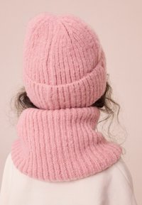 Rosa gestrickte Mütze mit geripptem Design und passendem Halswärmer, beide aus weichem, flauschigem Material für Wärme.