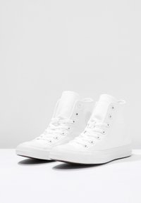 Baskets montantes en toile blanche avec semelles en caoutchouc, dotées d'œillets métalliques, de lacets ton sur ton et d'un patch logo circulaire sur le côté extérieur.