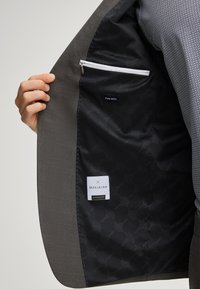 Gray wool blazer with patterned black lining. Inside features a zip pocket and labels for "Pure Wool" and "Officina." Smooth texture.