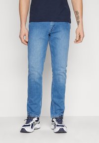 Blauwe denim jeans met een rechte pijp, lichte wassing en subtiele vervaging, gecombineerd met witte en marineblauwe sportschoenen.