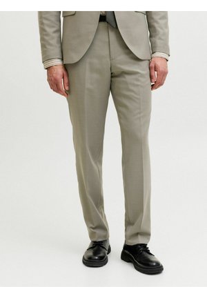 Homme portant un pantalon de costume gris clair, un blazer assorti, une chemise rayée, une ceinture noire et des chaussures habillées noires, debout sur un fond blanc.