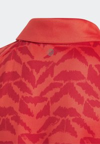 Kragskjorta i ljusröd tyg med ett subtilt lövmönster, slät textur och en liten logotypdetalj nära kragen.