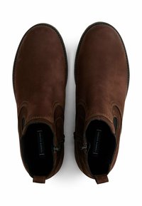 Un paio di stivali ankle in pelle marrone con cerniere laterali, pannelli elastici neri e soletti con marchio, visti dall'alto su uno sfondo bianco.