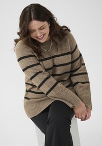 Pull à rayures marron en matière douce, avec des rayures noires, un ourlet côtelé et des manches amples, porté avec un pantalon noir.