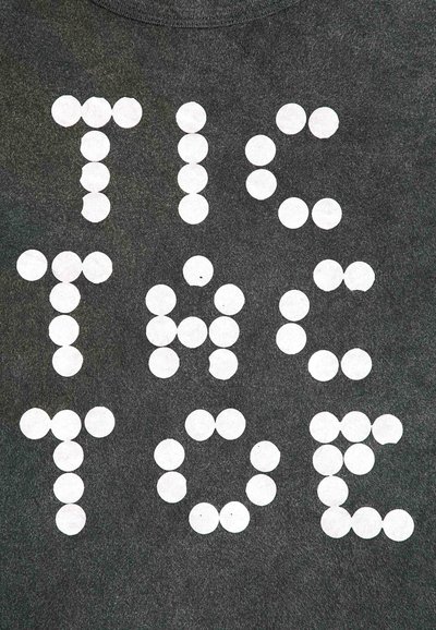 Grijze T-shirt met witte cirkelvormige vormen die de tekst "TIC TAC TOE" in vette letters vormen. De stof lijkt zacht en gestructureerd.