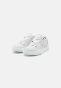 Hvite sneakers med overdel i teksturert lær, perforerte sider, flate lisser og gummisåle. Enkel design med minimal detaljer.