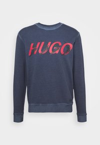 Felpa blu navy con polsini e orlo a coste, caratterizzata dalla scritta "HUGO" in grassetto, stile graffiti rosso e nero, sulla parte anteriore.