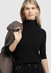 Črna, prilega se telesu, pulover s turtleneck ovratnikom in tričetrtinskimi rokavi. Gladka tekstura, v paru s sivo jakno, ki jo drži čez ramo.