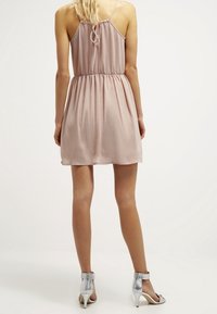 Robe rose clair sans manches avec une taille cintrée et une jupe fluide. Dotée d'un nœud à l'arrière et d'un tissu lisse et doux. Talons argentés complètent le look.