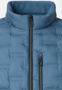 Blaue Steppjacke mit hohem Kragen, zwei schwarzen Reißverschlüssen und gesteppter Struktur. Der Stoff wirkt glatt, mit einem atmungsaktiven Innenfutter aus Mesh.