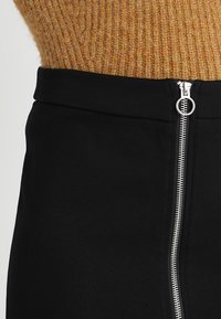 Černá sukně s bočním zipem se stříbrným kováním, vyrobená z hladké látky. Pas je přiléhavý a bez švů.