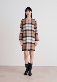 Ruudu dress pikade varrukatega, millel on beeži, pruuni ja mereväe toone. Valmistatud pehmest kangast, sirge lõikega ja põlvepikkuses. Mustad saapad.