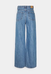 Jean en denim bleu taille haute à jambes larges, avec poches arrière et une étiquette de marque en cuir marron sur la ceinture.