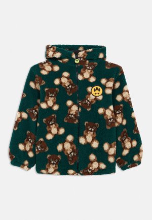 Sötétzöld bolyhos dzseki barna mackó mintával, kapucnival, elöl cipzárral, és egy sárga folttal, fekete mancspatróval a mellkason.