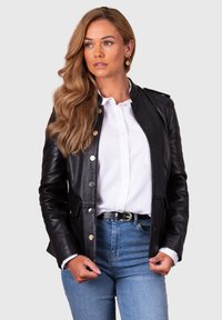 Black leather jacket with silver buttons, a tailored fit, and a smooth texture, layered over a white collared shirt and blue jeans.