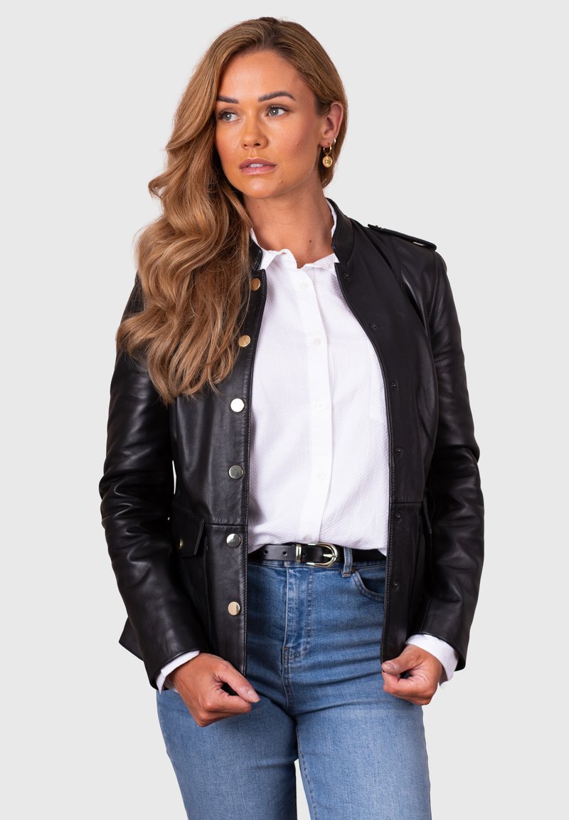 Black leather jacket with silver buttons, a tailored fit, and a smooth texture, layered over a white collared shirt and blue jeans.