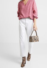 Roze v-halsblouse met zwarte spikkels, witte rechte jeans en enkellaarsjes met een slangenhuidpatroon. Kleine slangenhuidhandtas met korte handgreep.