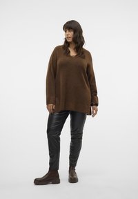 Brown oversized sweater with long sleeves, paired with black leather pants and brown ankle boots. Smooth texture and relaxed fit.
