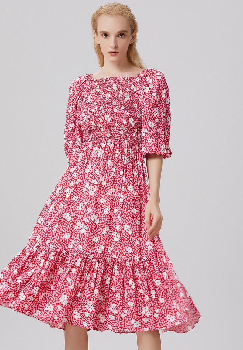 Robe rouge à fleurs avec des manches bouffantes et un corsage smocké. Elle présente une jupe à volants en étages, fabriquée à partir d'un tissu léger et fluide.