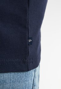 Marineblauw katoenen T-shirt met korte mouwen, voorzien van een klein geborduurd logo op de zoom en zichtbare naden langs de onderkant.