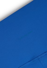 Niebieska tkanina sportowa, gładka tekstura, dopasowany krój, z subtelnym logo w lekko ciemniejszym odcieniu niebieskiego oraz widocznymi detalami szwów.