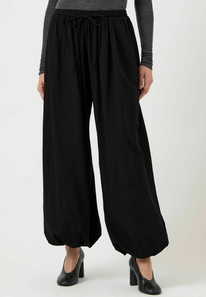 Czarne spodnie o szerokich nogawkach wykonane z lekkiego materiału, z elastycznym paskiem i sznurkiem do regulacji oraz marszczonymi mankietami przy kostkach.