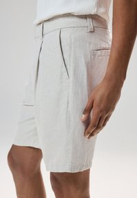 Shorts en lin gris clair avec une taille cintrée, des plis à l'avant, des poches latérales et un ourlet net. Texture douce et tissu respirant.
