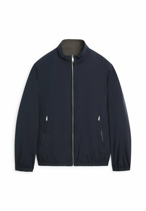 Veste légère bleu marine avec fermeture éclair frontale, col montant, poignets élastiques et deux poches latérales zippées sur fond blanc.