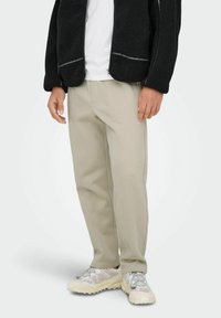 Black fleece jacket with zipper, paired with beige trousers featuring side pockets. Light-colored, chunky sneakers complete the outfit.