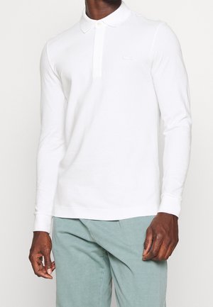 Biała longsleeve polo z zapięciem na guziki, ribbowanymi mankietami oraz małym haftowanym logo na piersi. Noszona z jasnoszarymi spodniami.