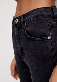 Jean en denim noir avec une texture lisse, taille haute et design à cinq poches. Doté de garnitures en argent et d'une silhouette ajustée.