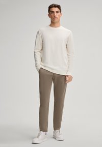 Langärmliges cremefarbenes Hemd, kombiniert mit hellbraunen Hosen und weißen Sneakers. Einfaches Design mit lockerer Passform und weicher Textur.